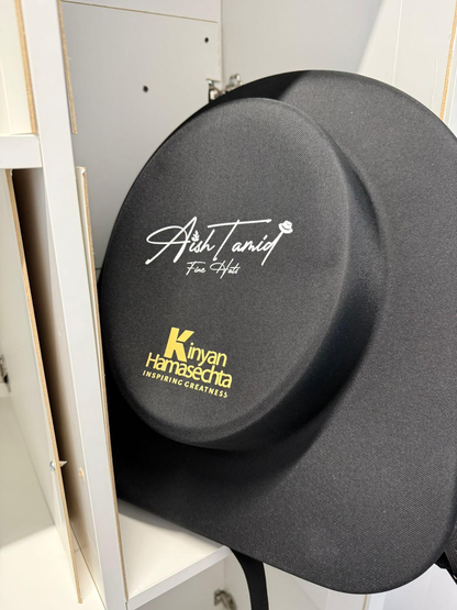 Aish Tamid hat travel bag with the gold Aish Tamid Fine Hats emblem and a customer's Kinyan Hamasechta logo printed beneath it